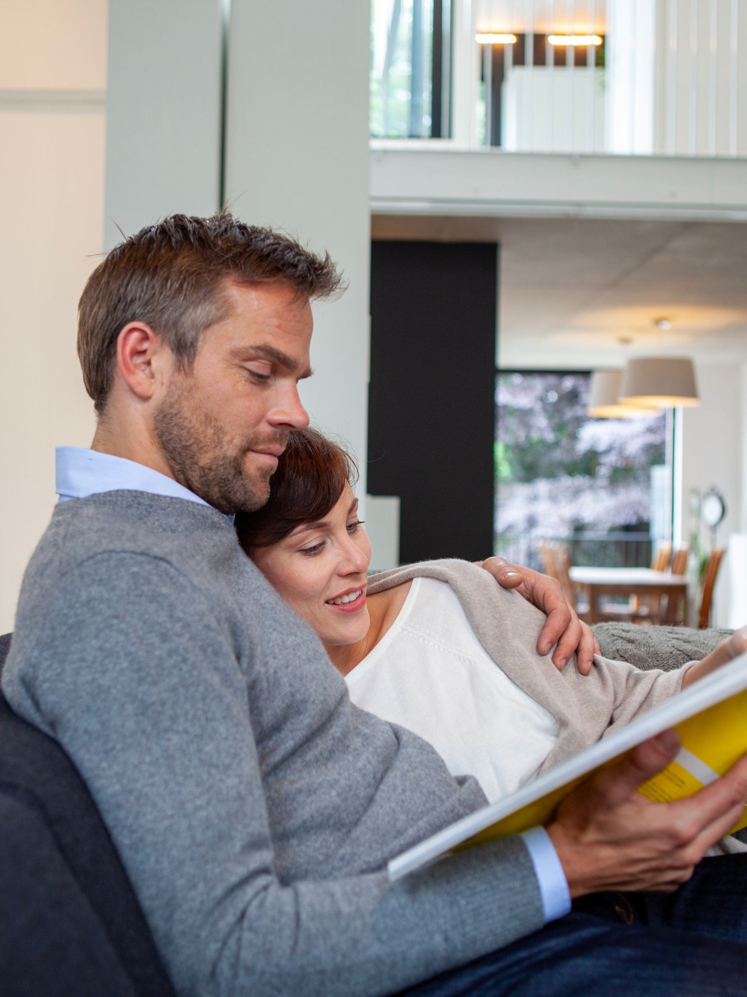 Et par krammer og slapper af i sofaen, mens de læser en bog i en perfekt temperatur.