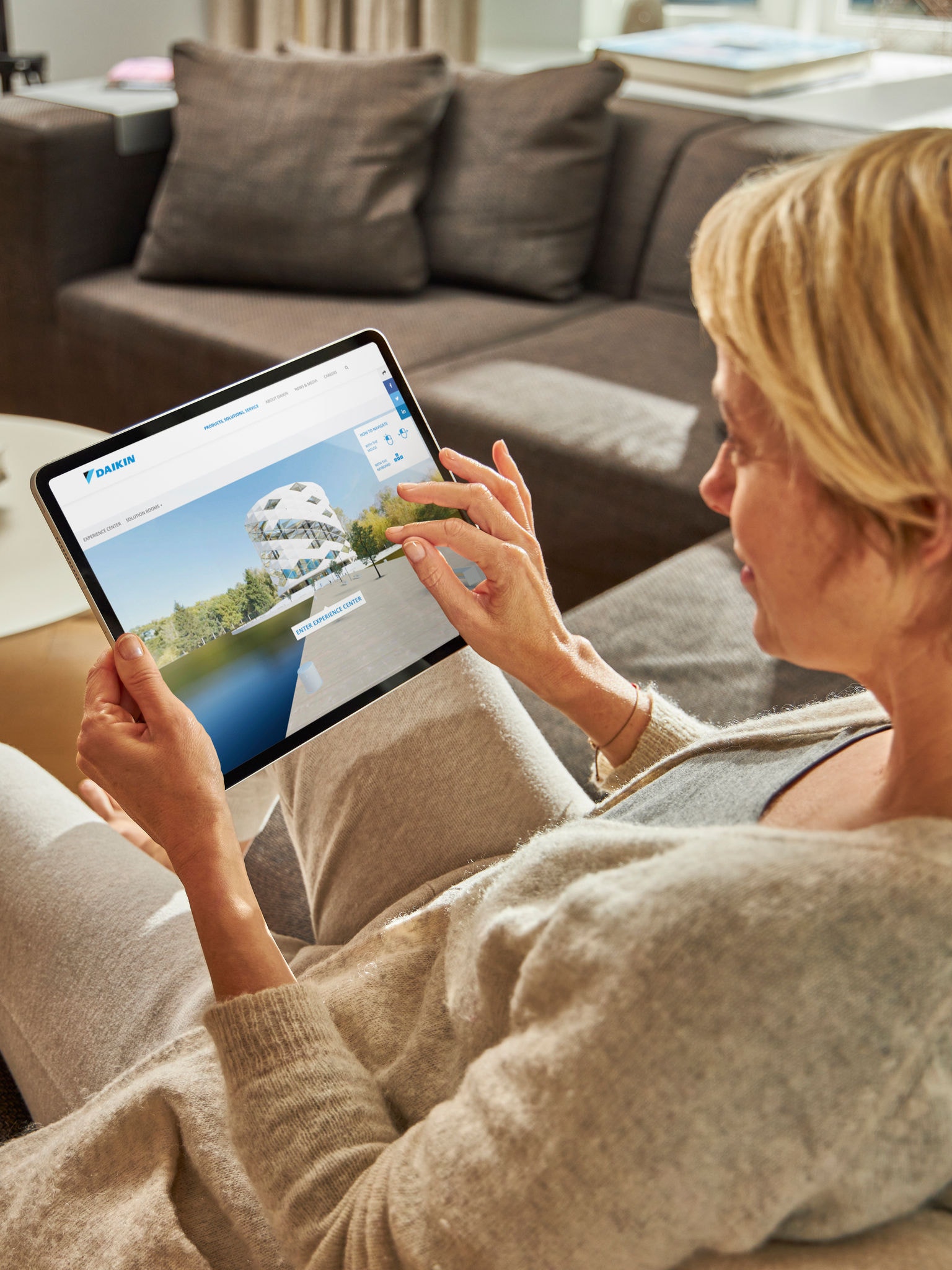 En kvinde besøger det virtuelle oplevelsescenter på sin tablet, mens hun slapper af i sofaen.