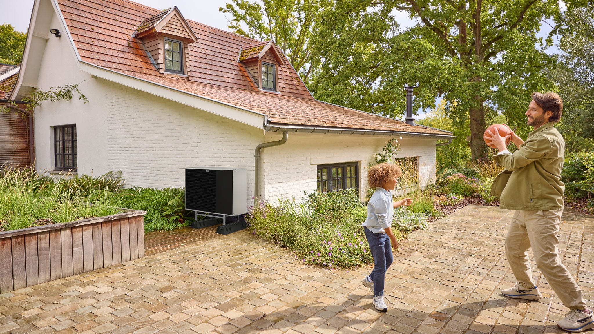 En far spiller bold med sin søn udendørs i nærheden af en varmepumpe