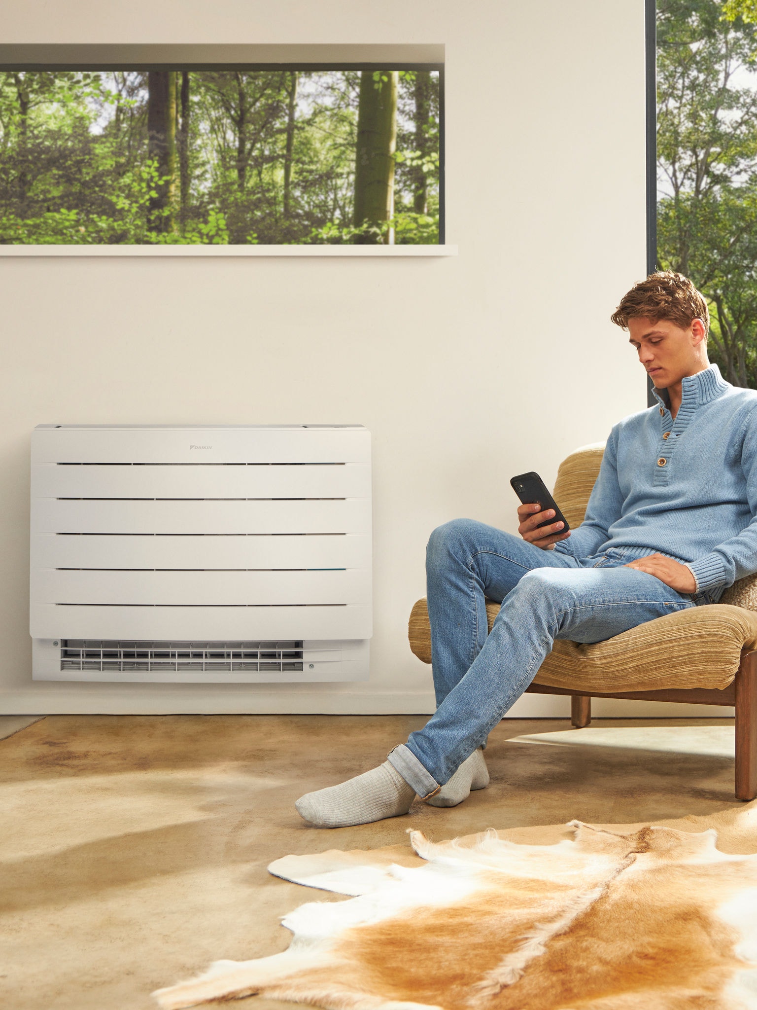 En mand sidder i et rum og kigger på sin telefon, og på væggen bag ham hænger der en varmepumpe