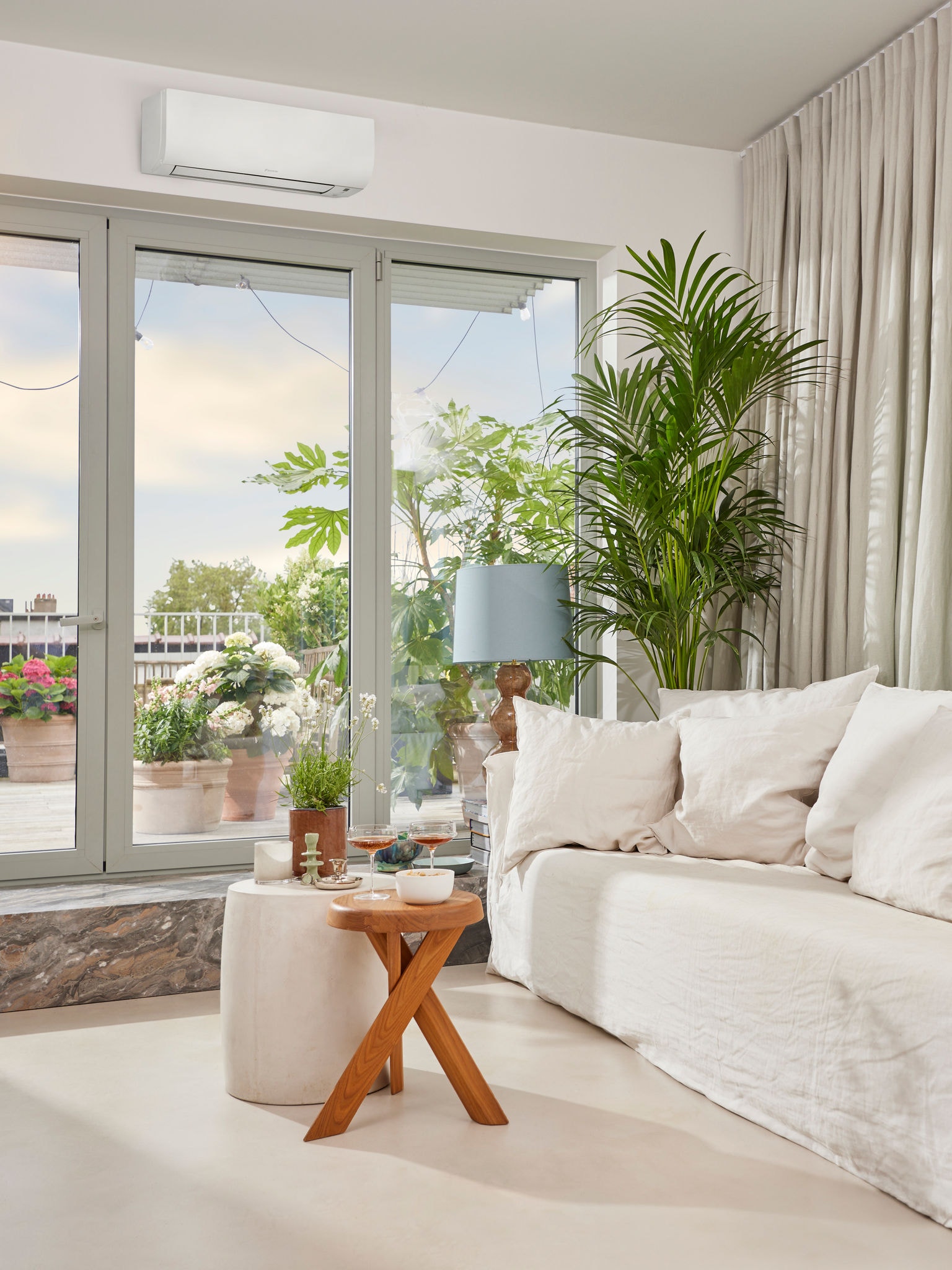 Lys og rar opholdsstue, hvor der er dækket op med aperitiffer, et klimaanlæg hænger over store glasdøre, som leder ud til en terrasse.