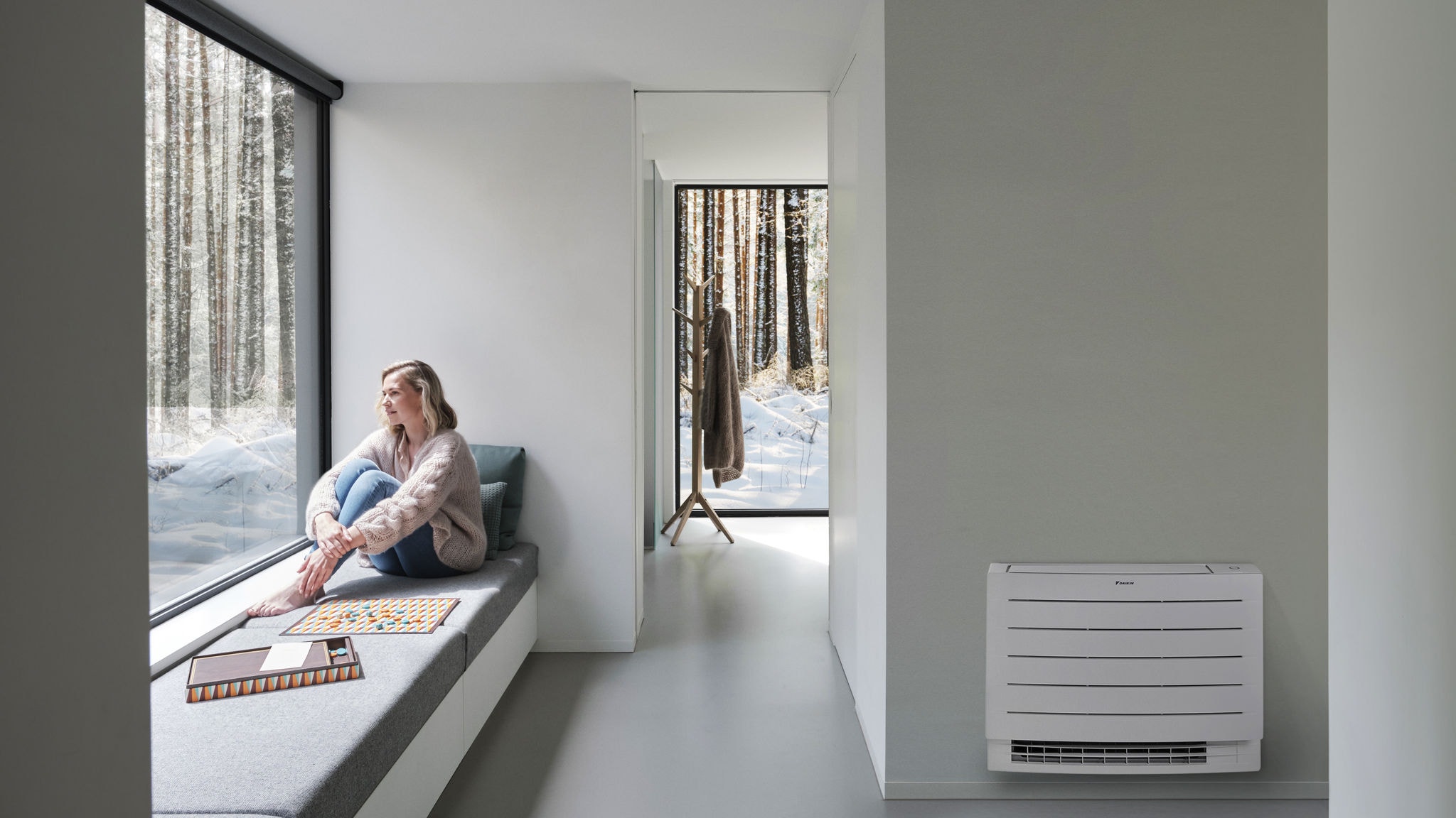 En kvinde kigger ud på sneen uden for sit hus, mens hun nyder et opvarmet hjem takket være en gulvplaceret Perfera-enhed.