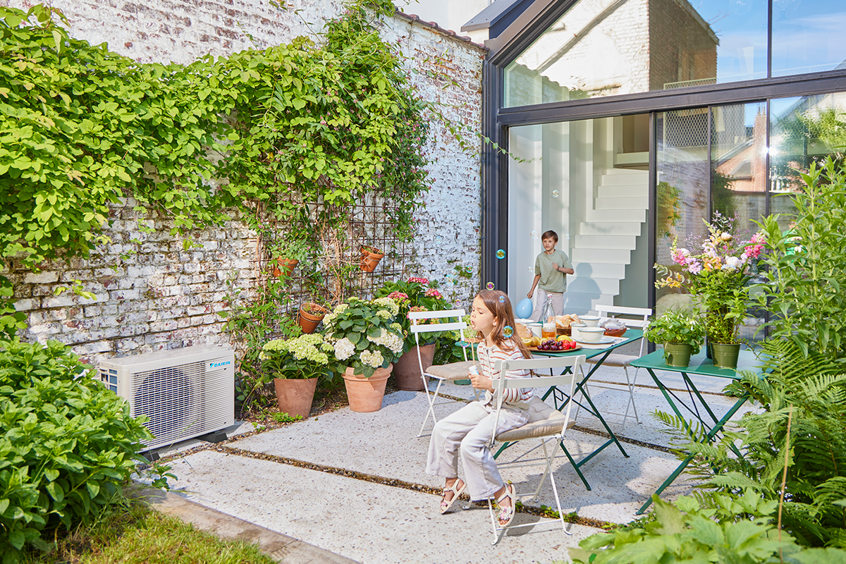 Børn leger med glaskugler på en terrasse ved siden af en udendørs varmepumpe