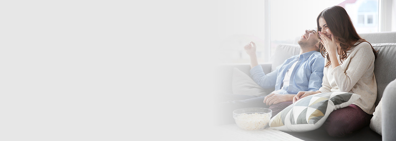 Leende par sidder i en sofa med popcorn.