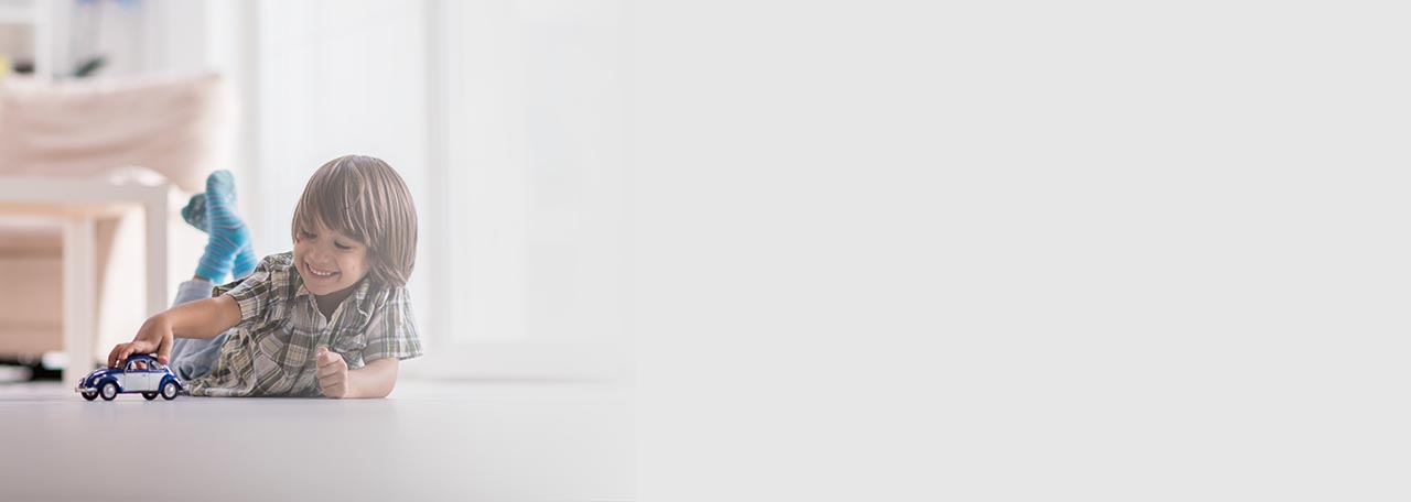 Dreng, der leger med en legetøjsbil på gulvet.