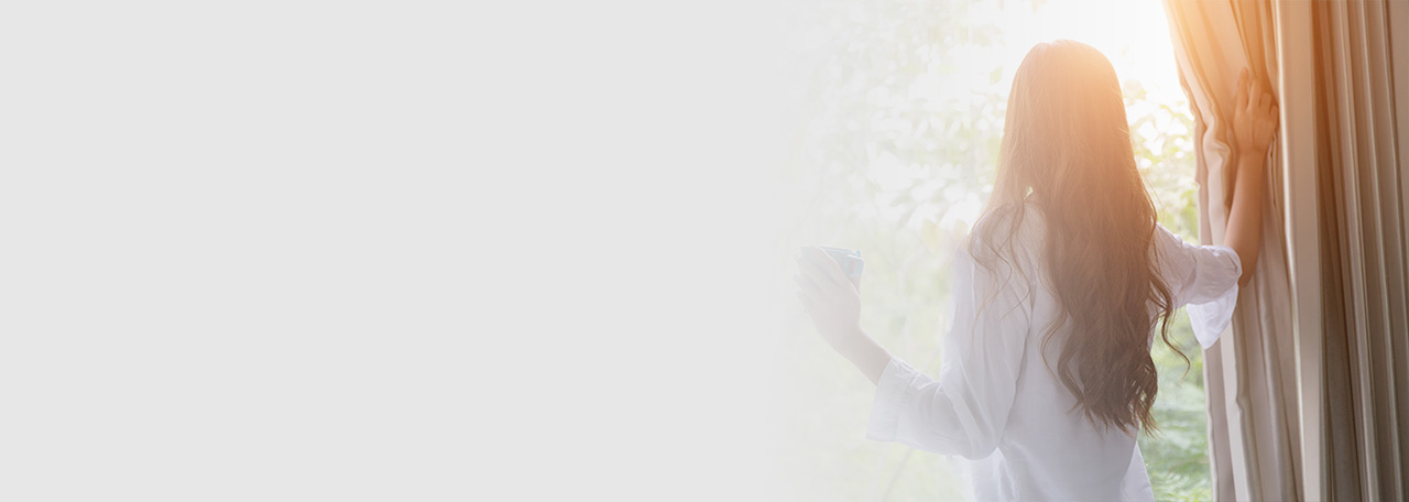Kvinde, der kigger ud, mens hun holder gardinet.