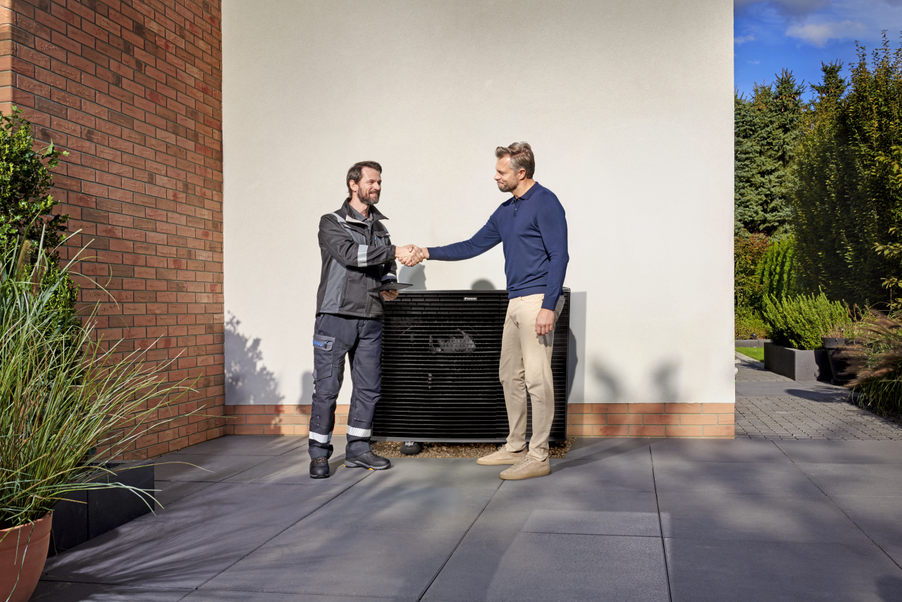 Installatøren om kunden giver hinanden håndtryk foran en Daikin Altherma-udendørsenhed